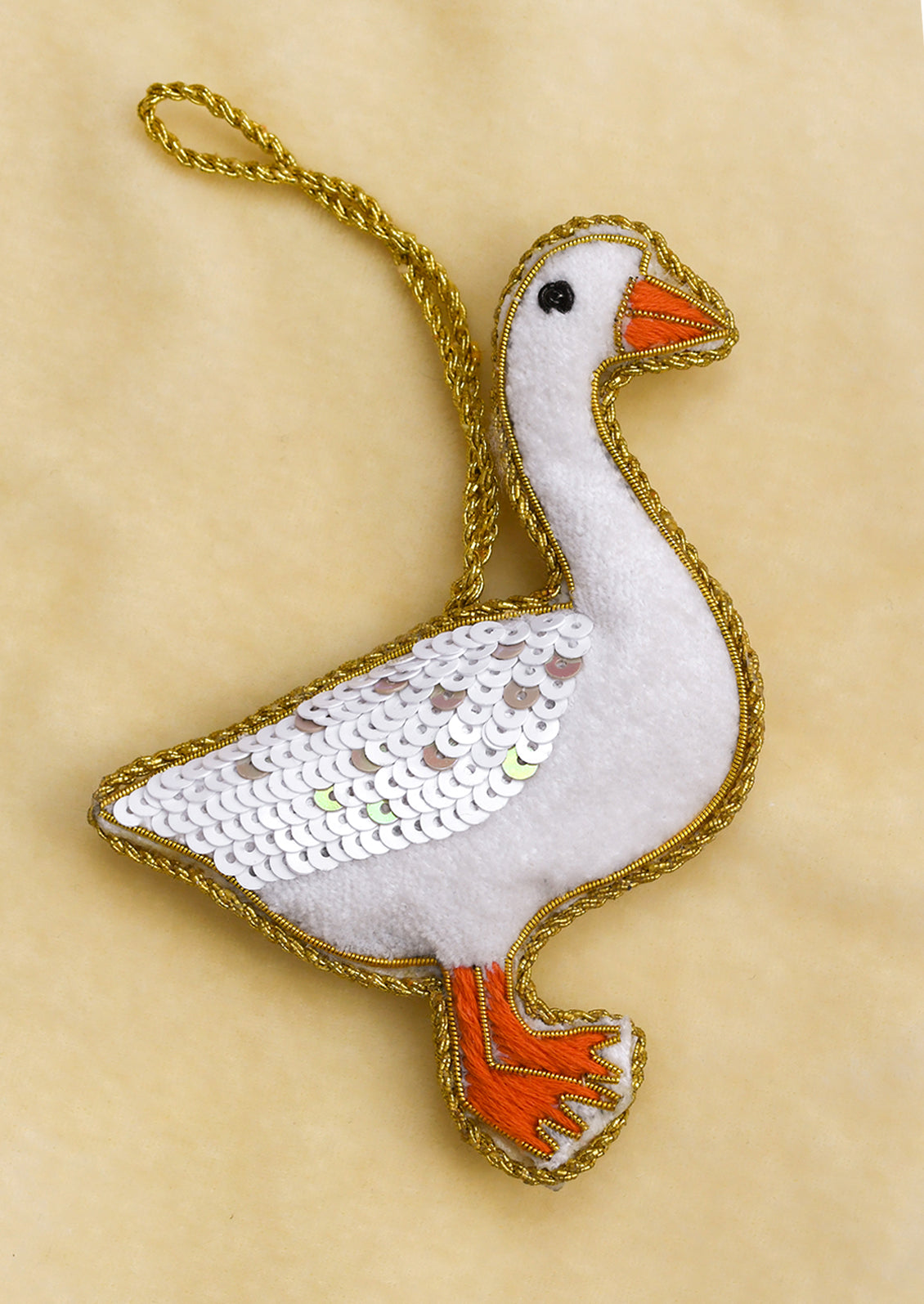 A soft fabric ornament in the likeness of a goose, adorned with gold embroidery and white sequins.