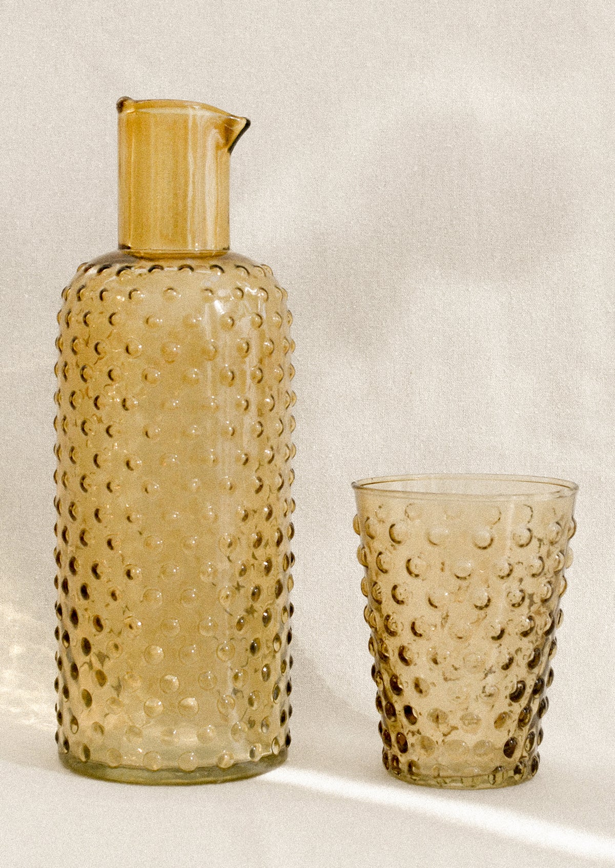 A carafe and cup set with hobnail texture in amber color.
