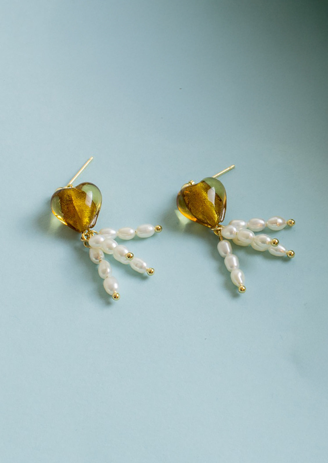 A pair of earrings with post stud, amber colored glass heart and pearl drop charms.