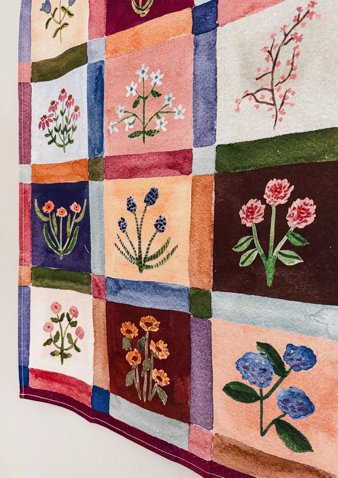 A cotton tea towel with colorful floral grid pattern.