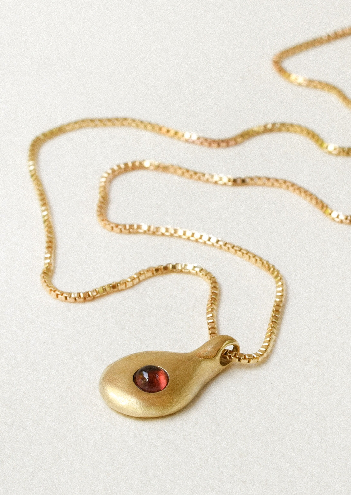 A bronze necklace with a droplet charm with a garnet on the front.