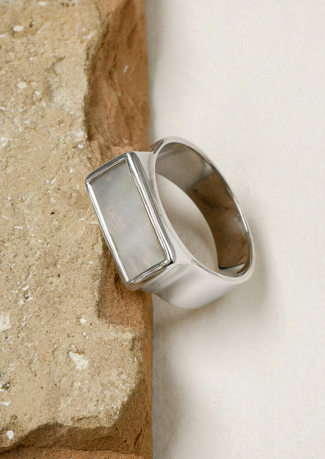 A sterling silver ring with a thick band and a rectangular mother of pearl set in the center, leaning on a brown stone.