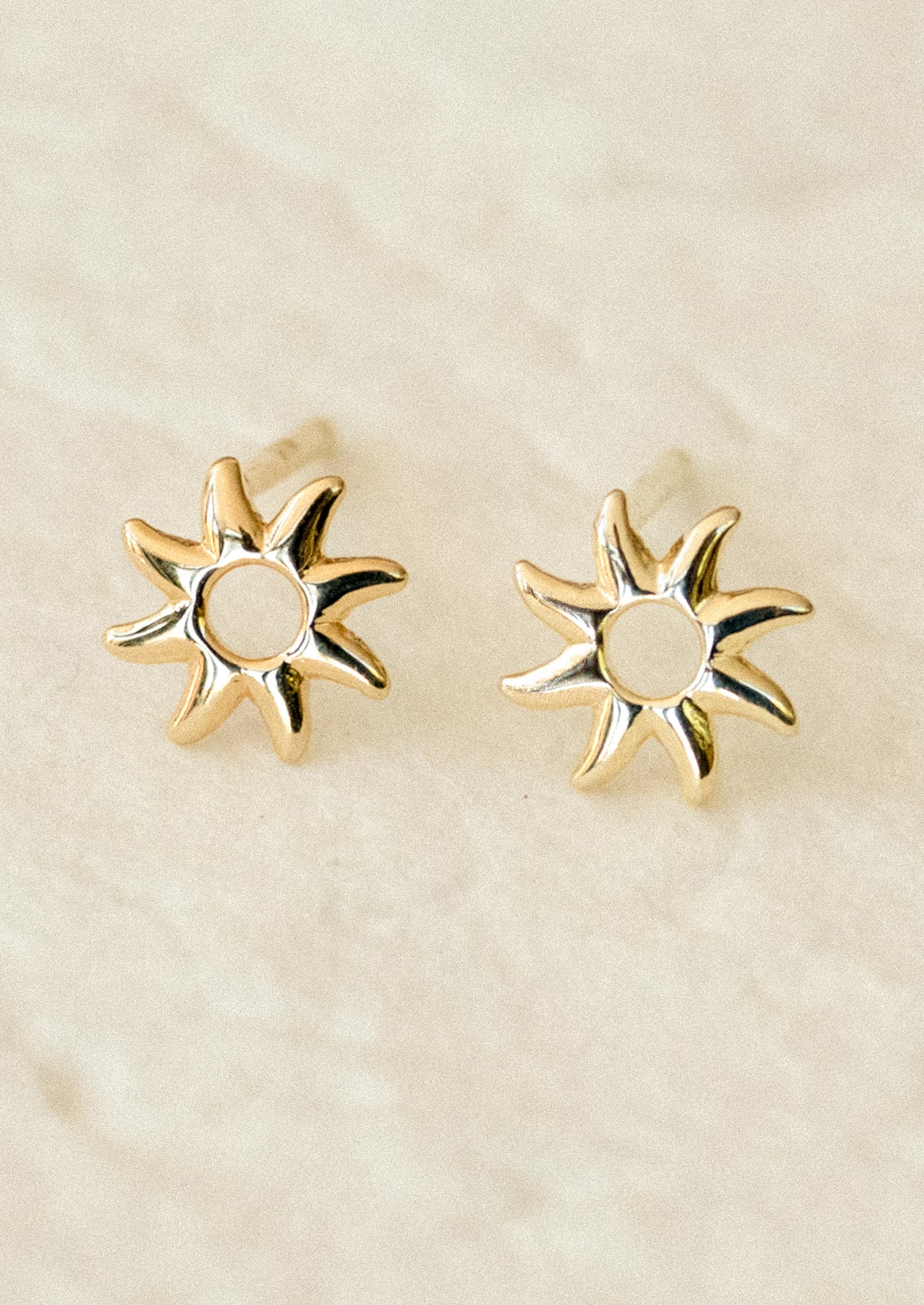 A pair of gold sun shaped stud earrings.