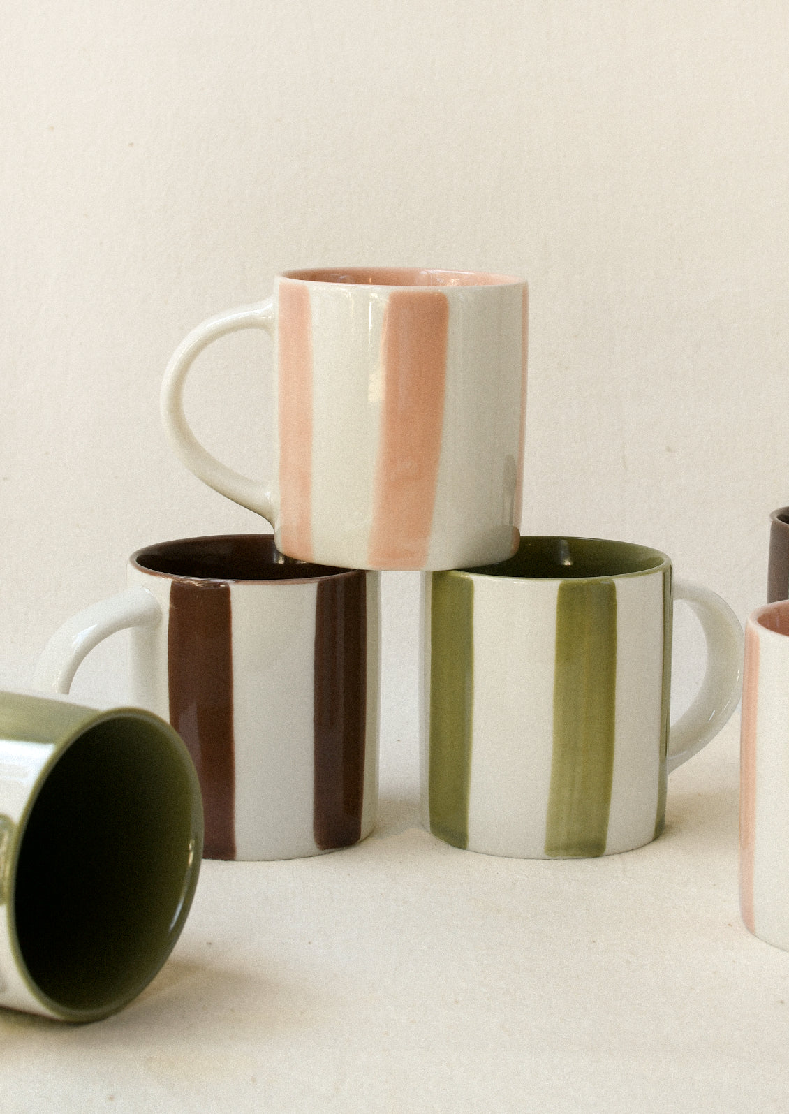 An assortment of small ceramic espresso cups with pink, green and brown stripes.