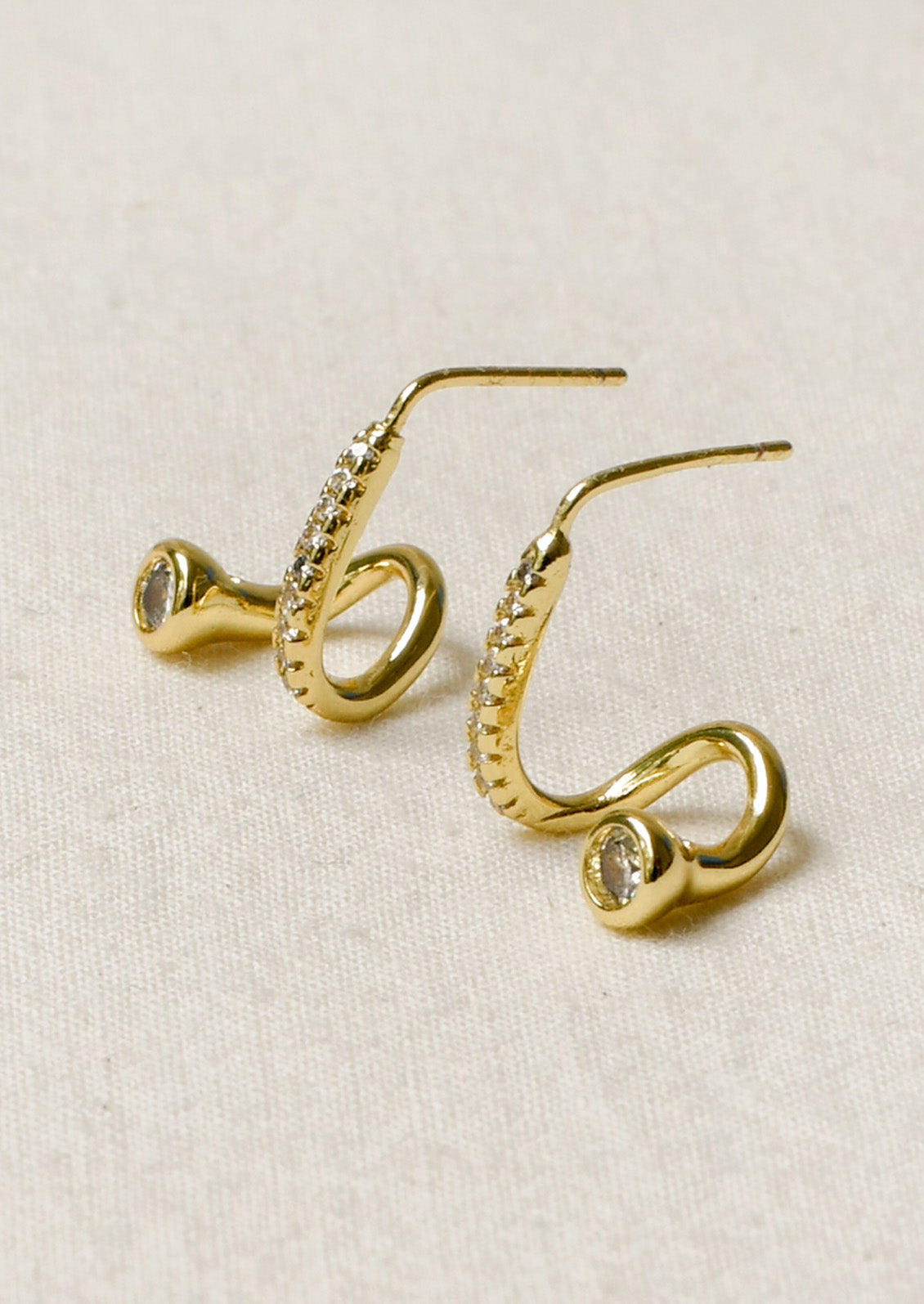 Side view of a pair of gold earrings in a unique sculpted design adorned with tiny cubic zirconias along the front.