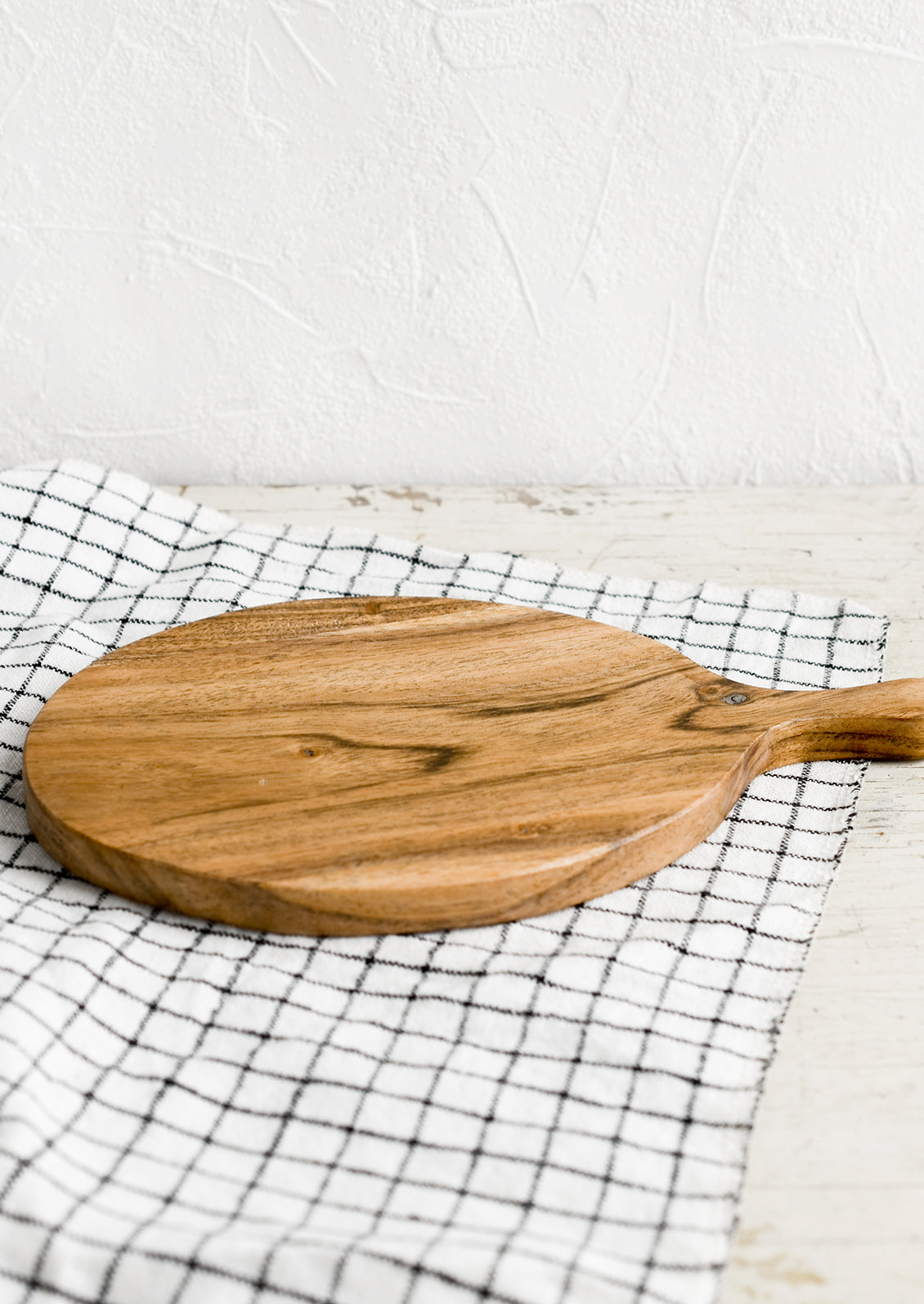 An oval shaped paddle-style cutting board in acacia wood.