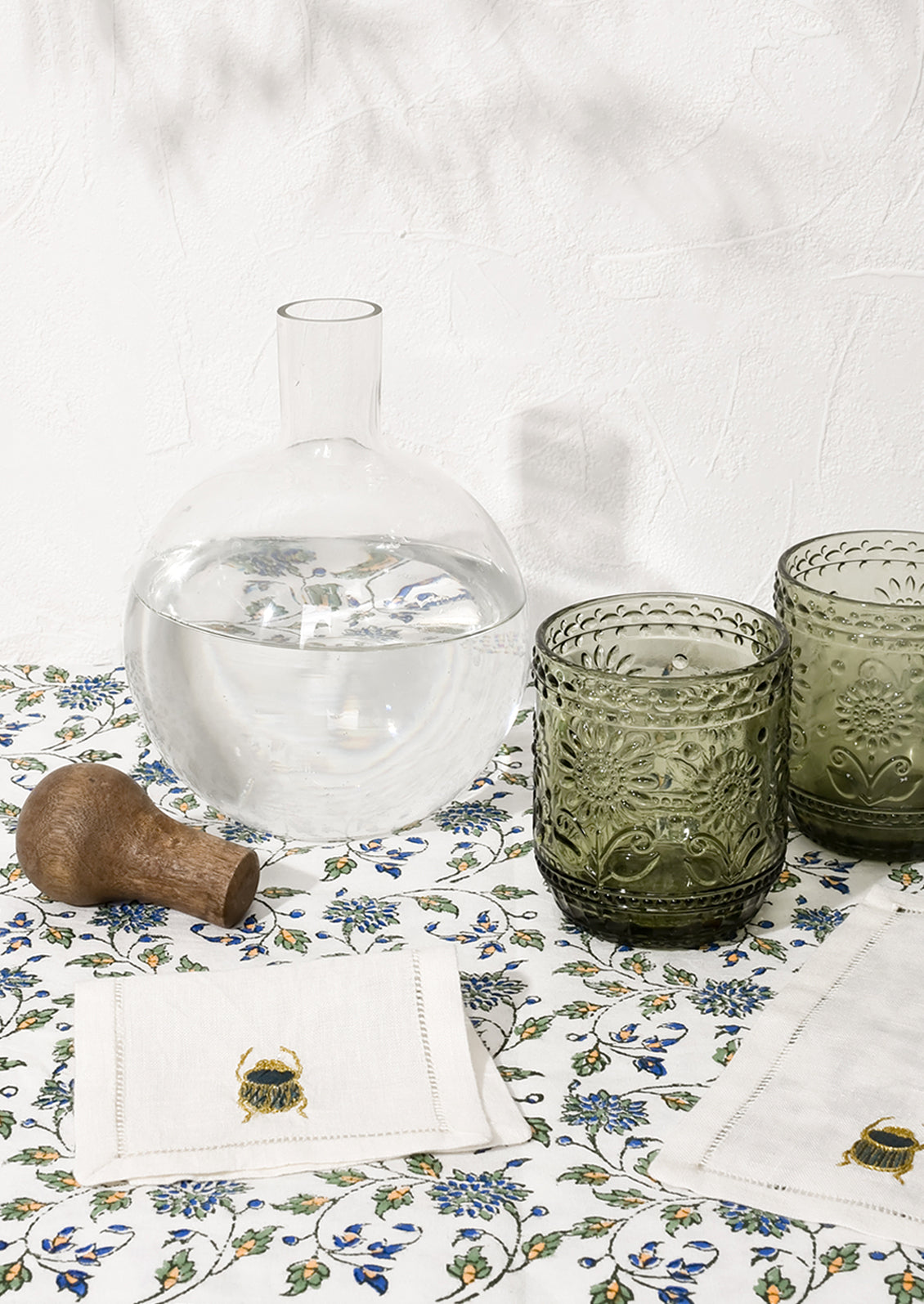 A glass decanter and cups pictured with scarab napkins.