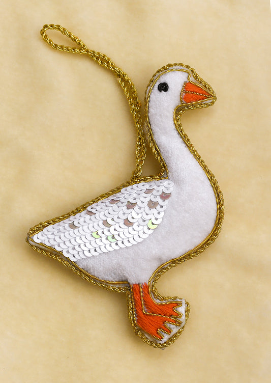 A soft fabric ornament in the likeness of a goose, adorned with gold embroidery and white sequins.