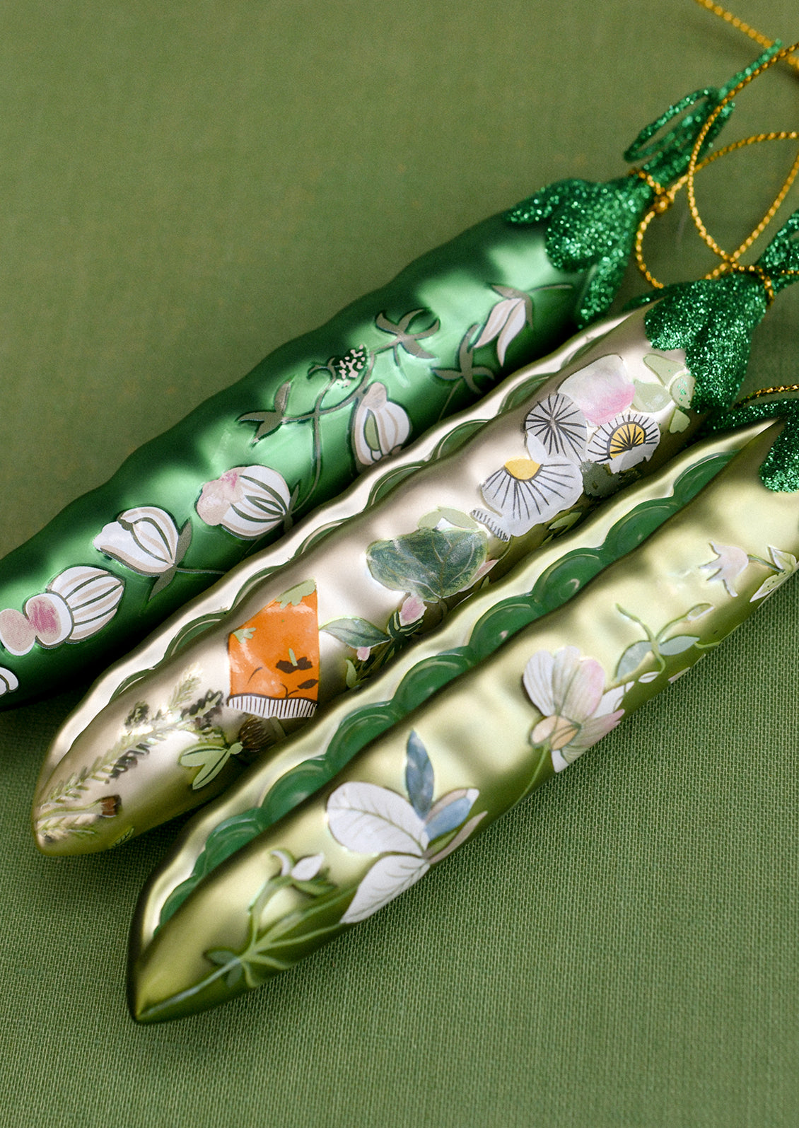 Glass ornaments depicting peapods with floral patterns on them.