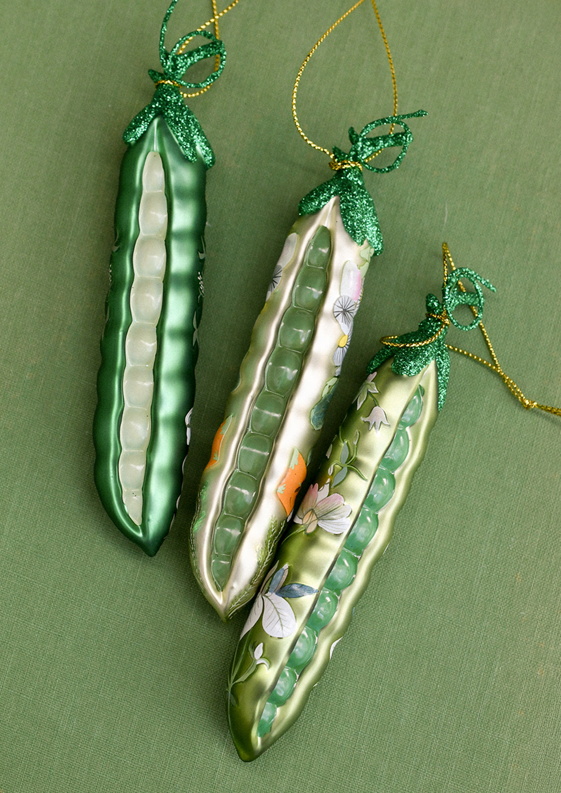 Glass ornaments depicting peapods with floral patterns on them.