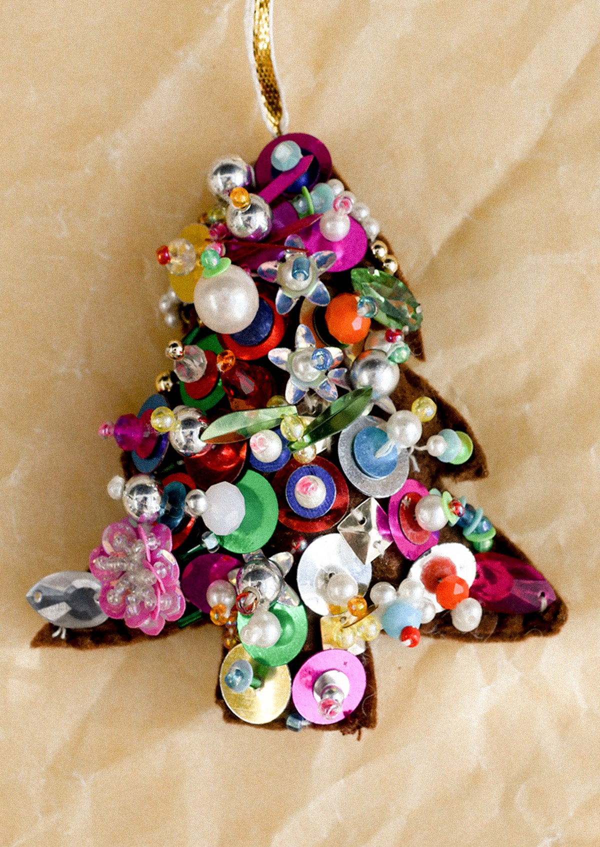 A soft holiday ornament in the shape of a christmas tree, decorated with an assortment of colorful beads and sequins.