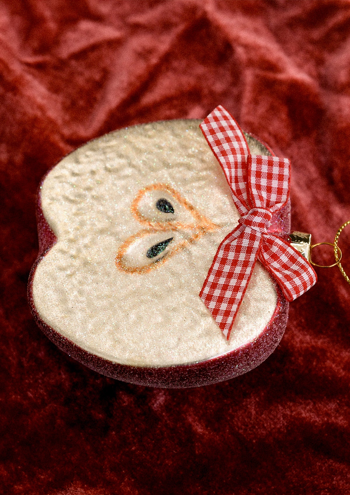 A glass ornament depicting a half apple, decorated with a red gingham bow.
