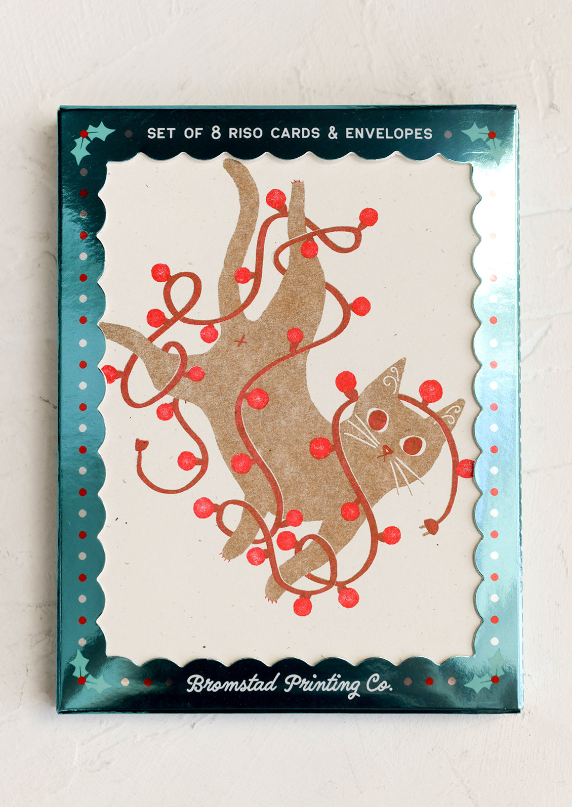 A boxed set of holiday greeting cards with a screenprinted image of brown cat tangled in red string lights.
