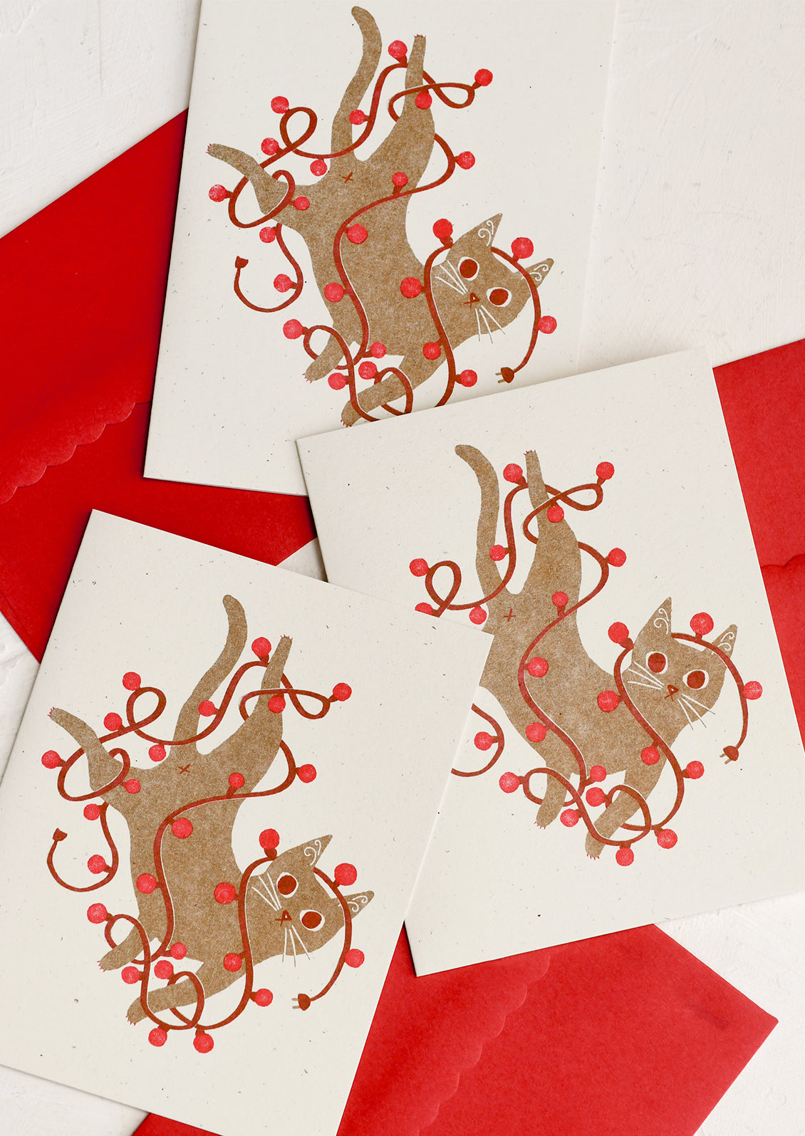 A set of holiday greeting cards with a screenprinted image of brown cat tangled in red string lights.