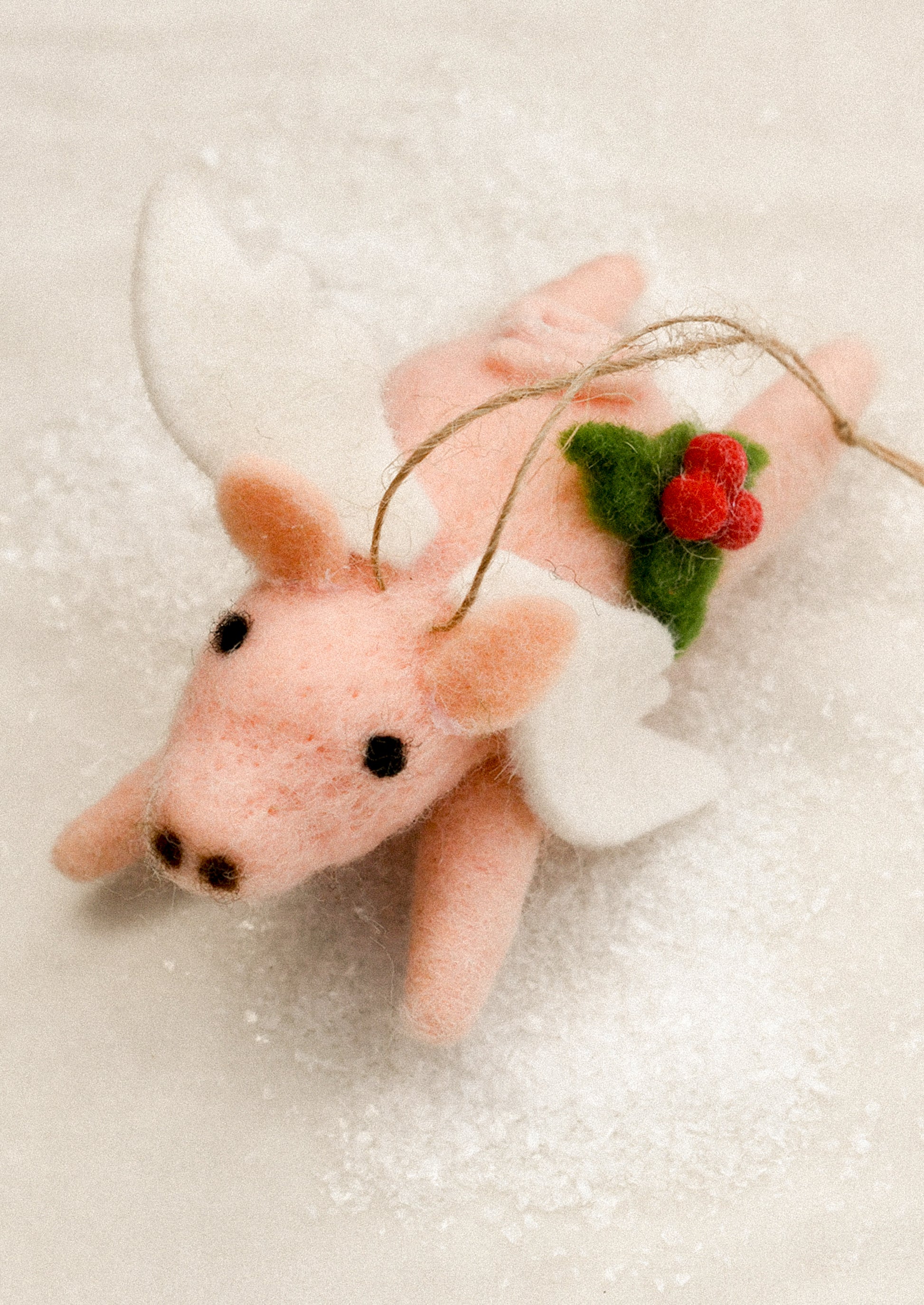 A felted pig ornament wearing angel wings, with holly decoration.