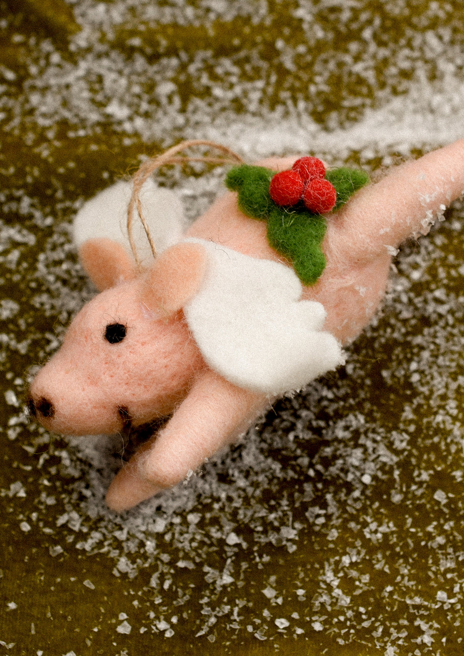 A felted pig ornament wearing angel wings, with holly decoration.