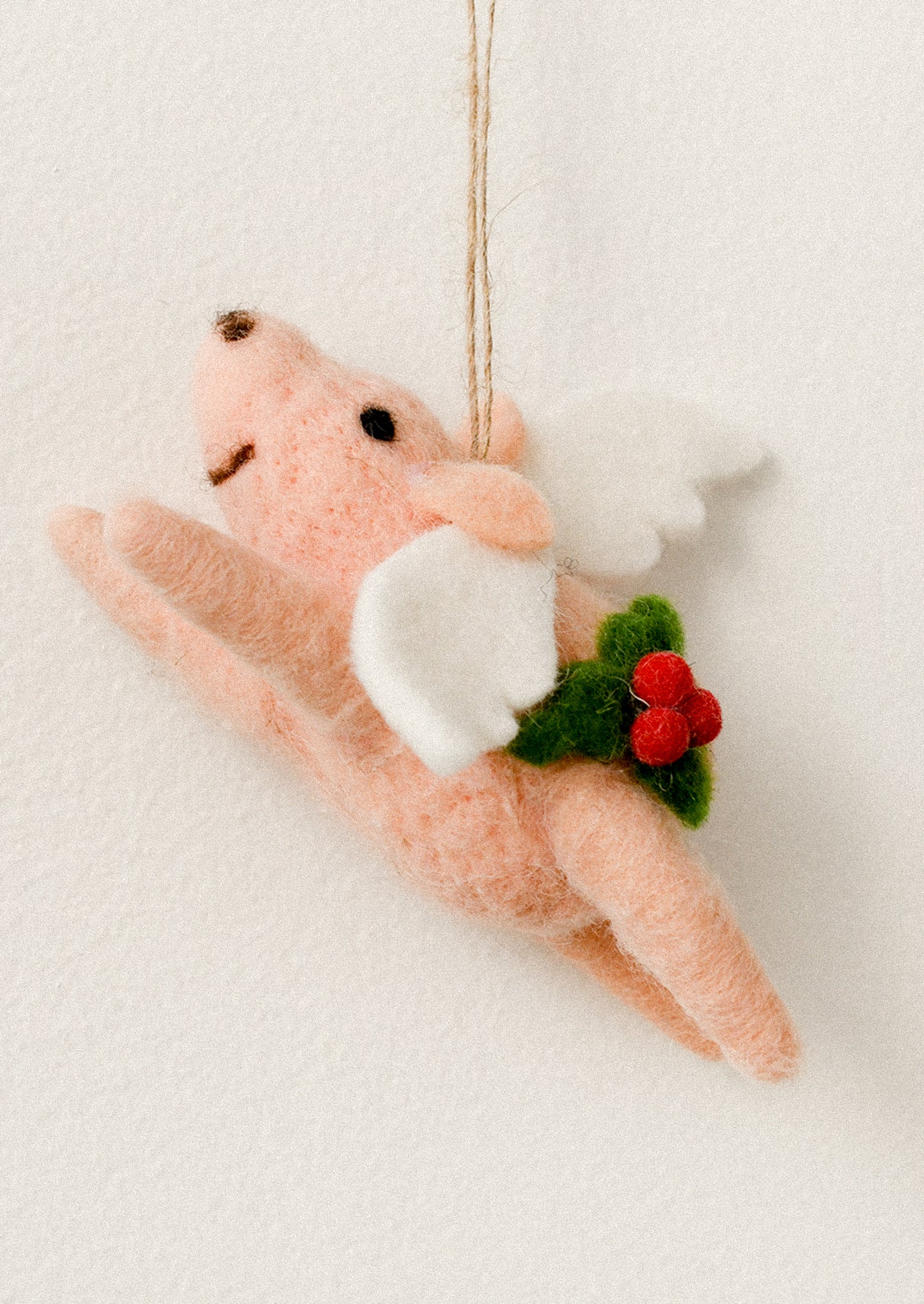 A felted pig ornament wearing angel wings, with holly decoration.