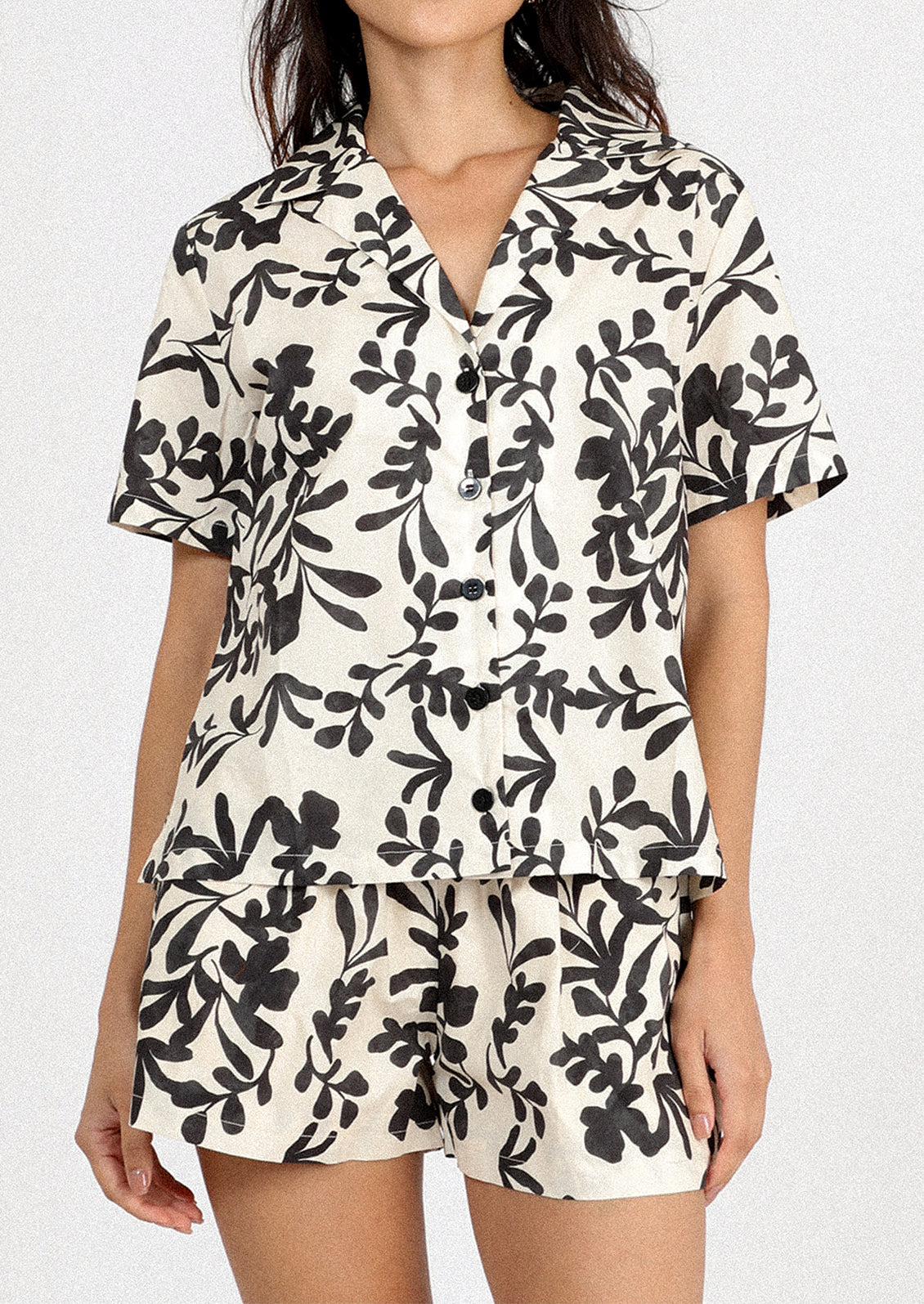 A person wearing a white short sleeve shirt with black leafy floral print.