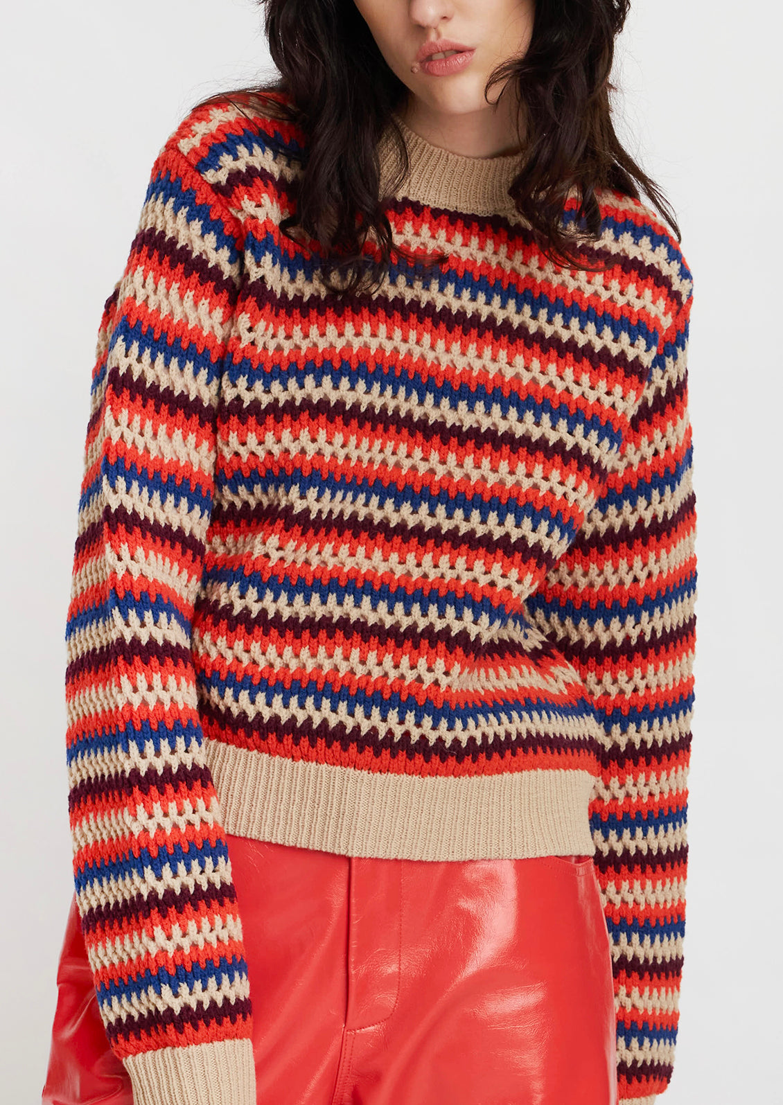 A woman wearing a crochet knit striped sweater in cream with orange, maroon and blue stripes.
