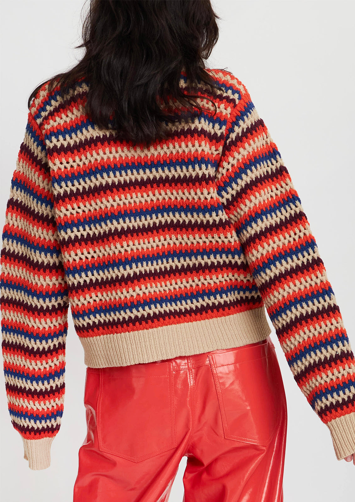 A woman wearing a crochet knit striped sweater in cream with orange, maroon and blue stripes.