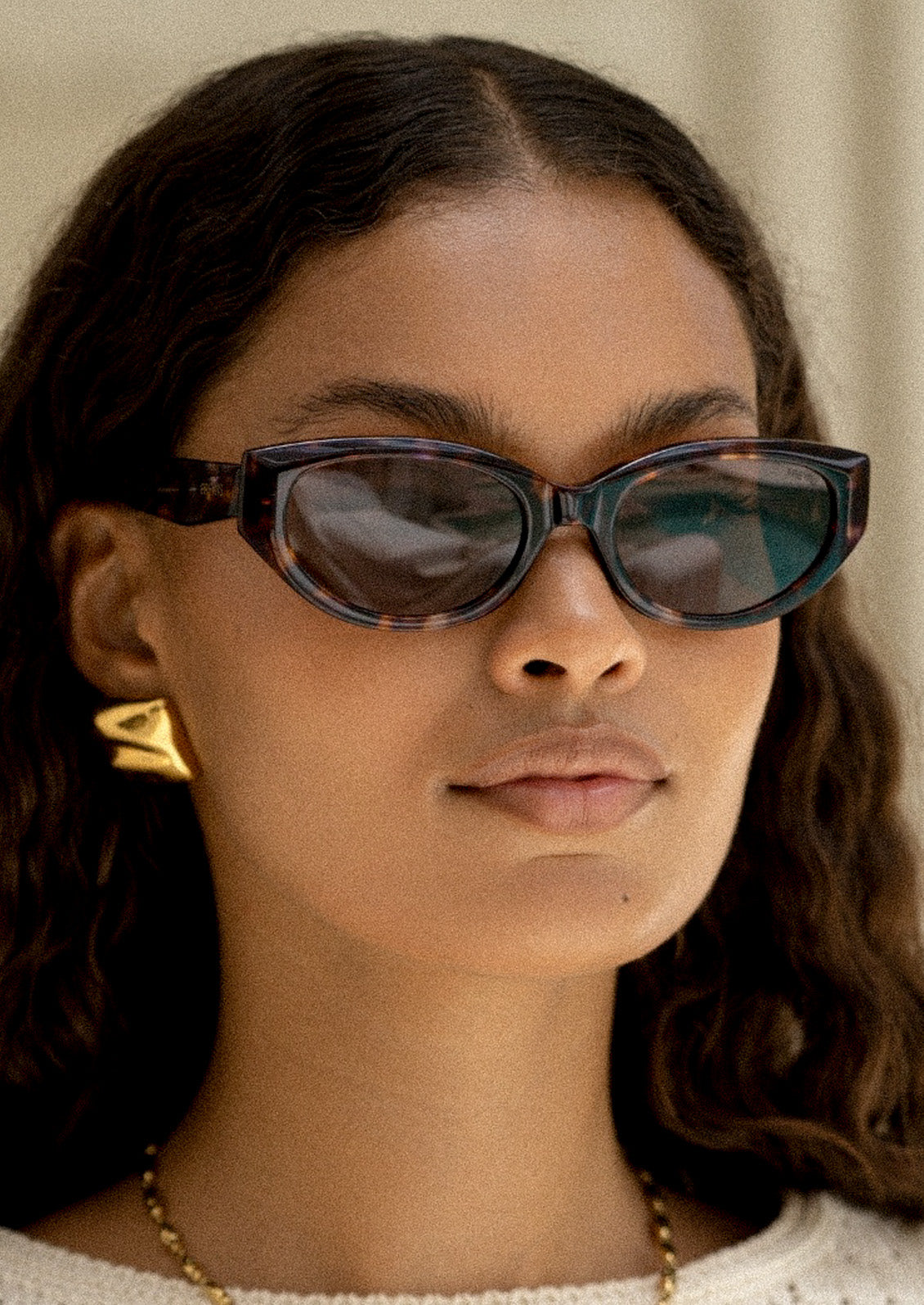A woman wearing a pair of cat eye sunglasses with marbled tortoise frames and brown tinted lenses.