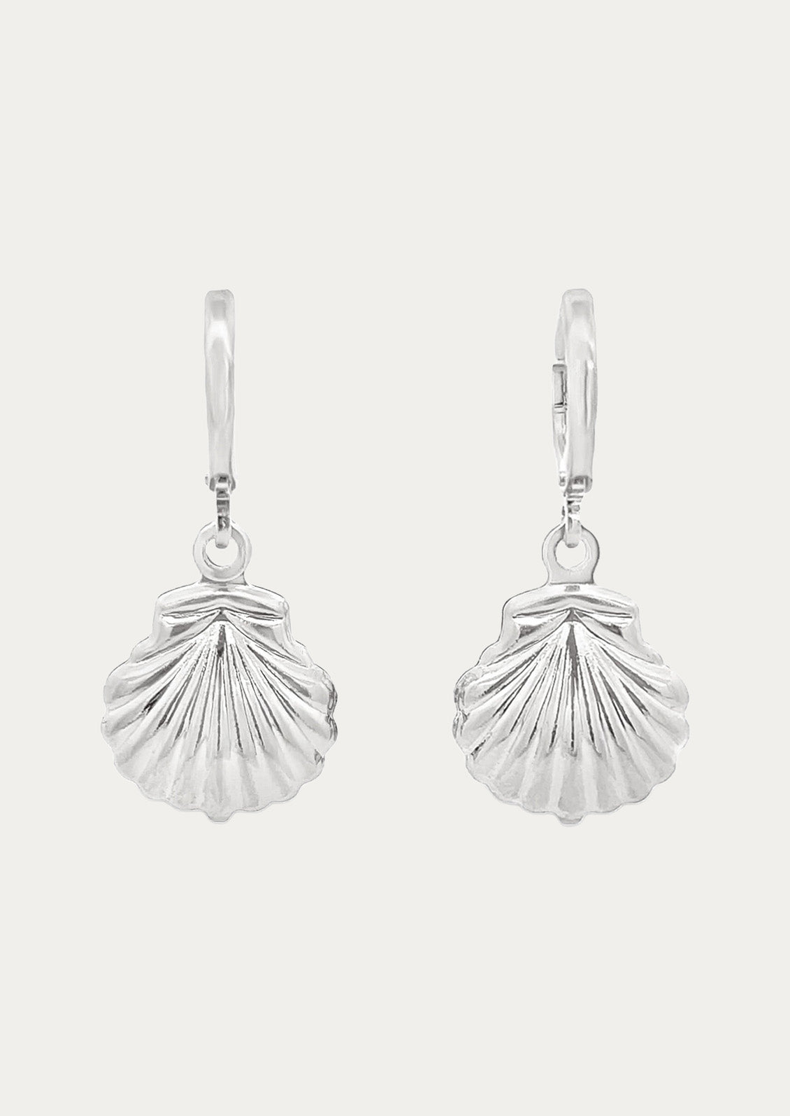 A pair of silver huggie hoop earrings with silver dangling seashell charms on a white background.