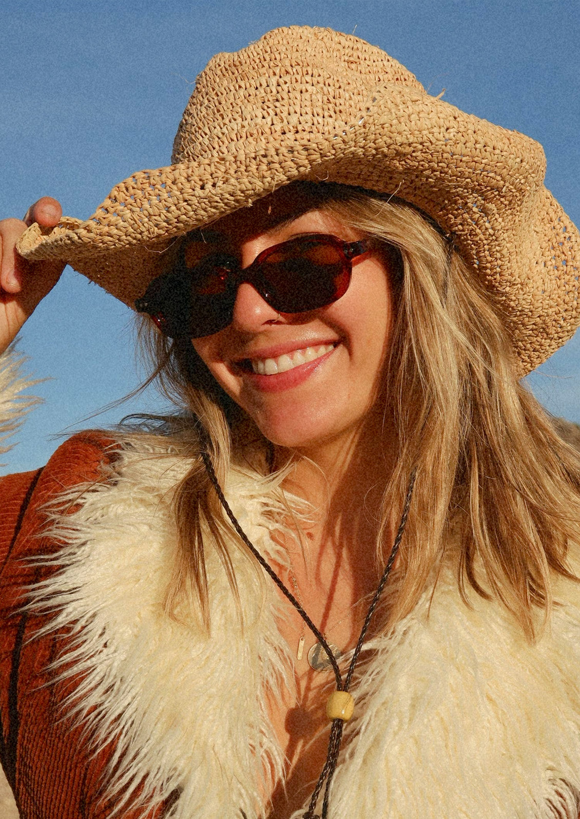 A woman wearing a pair of oval-rectangle sunglasses with a translucent cherry red frame and warm medium-brown tinted lenses.