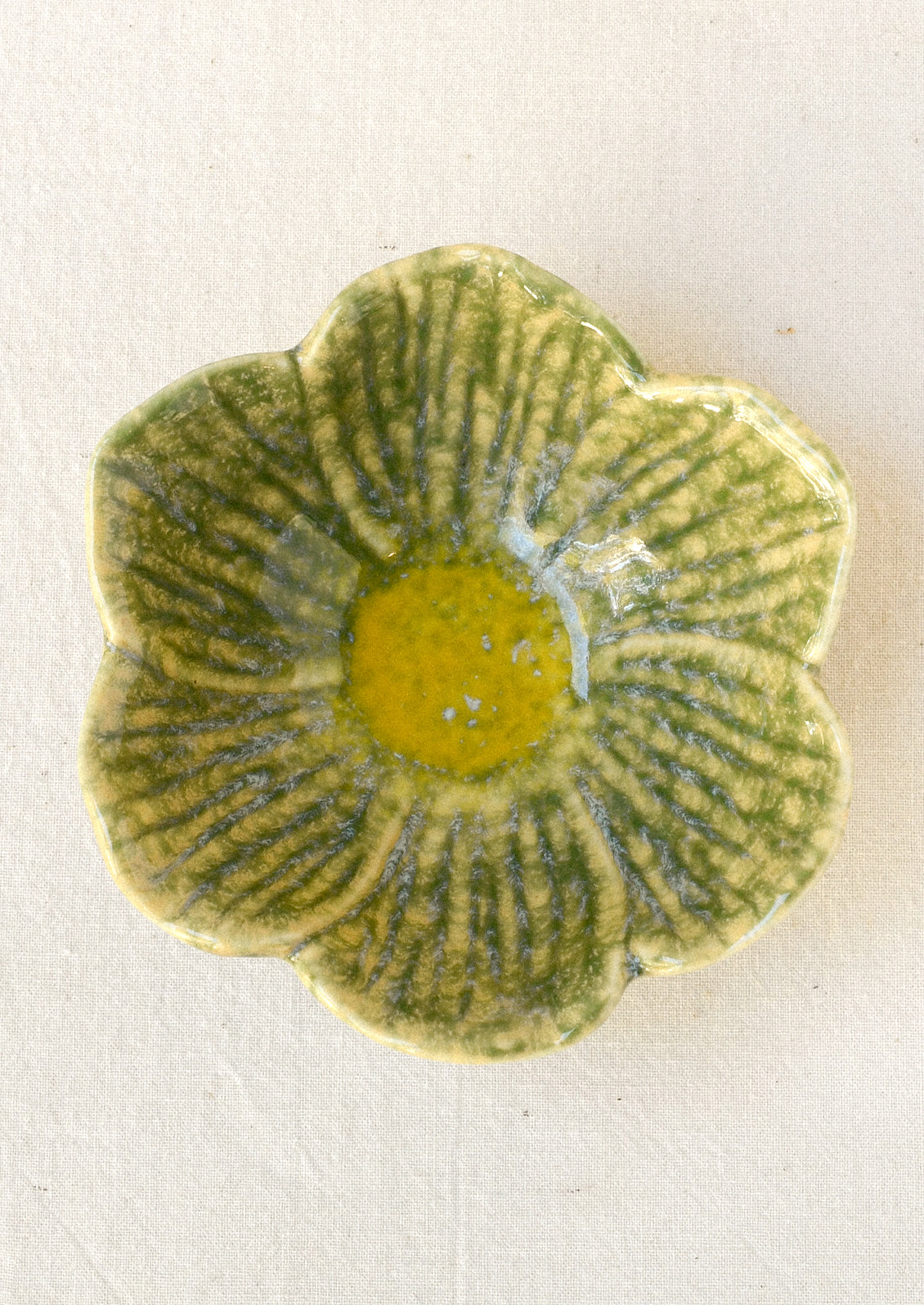 A small ceramic catchall bowl in the shape of a six petal flower in green with a yellow center.