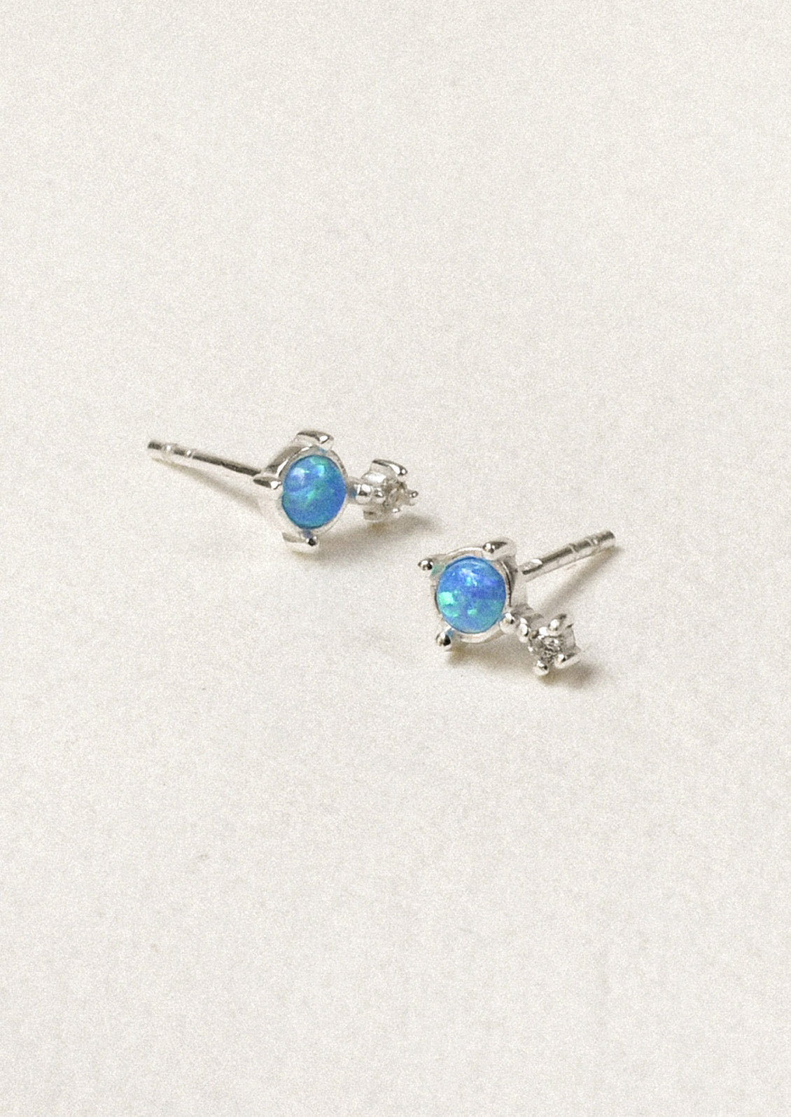 A pair of sterling silver stud earrings with a vibrant blue opal set in the center.