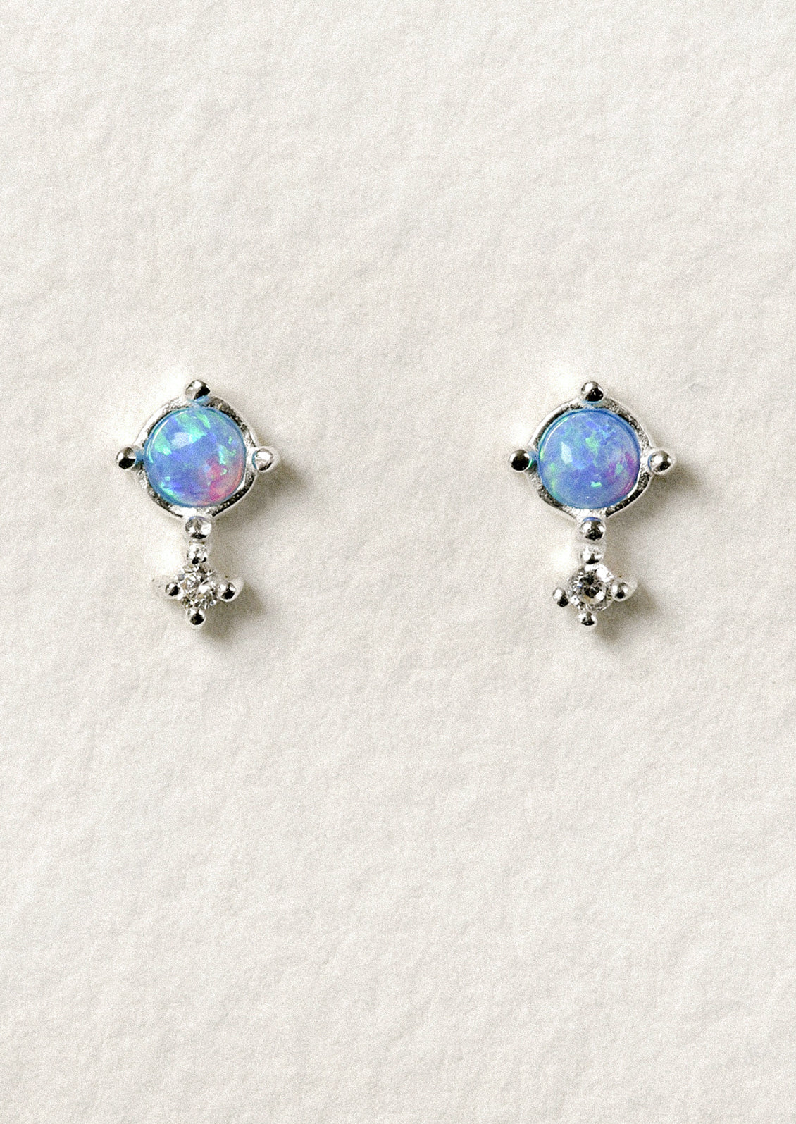 A pair of sterling silver stud earrings with a vibrant blue opal set in the center.