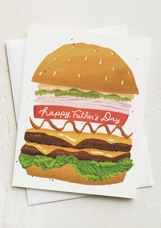 A greeting card with illustration of tall cheeseburger, "Happy Father's Day" text across tomato slice.