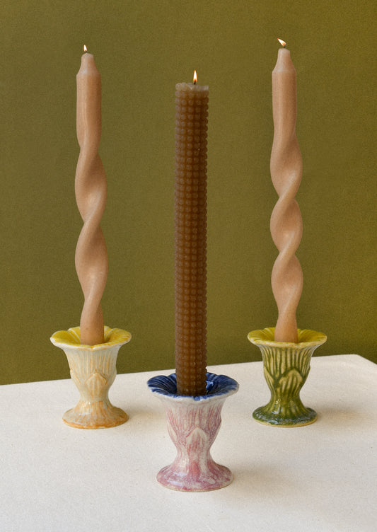 Three colorful flower-shaped ceramic taper candle holders each with a lit candle. 