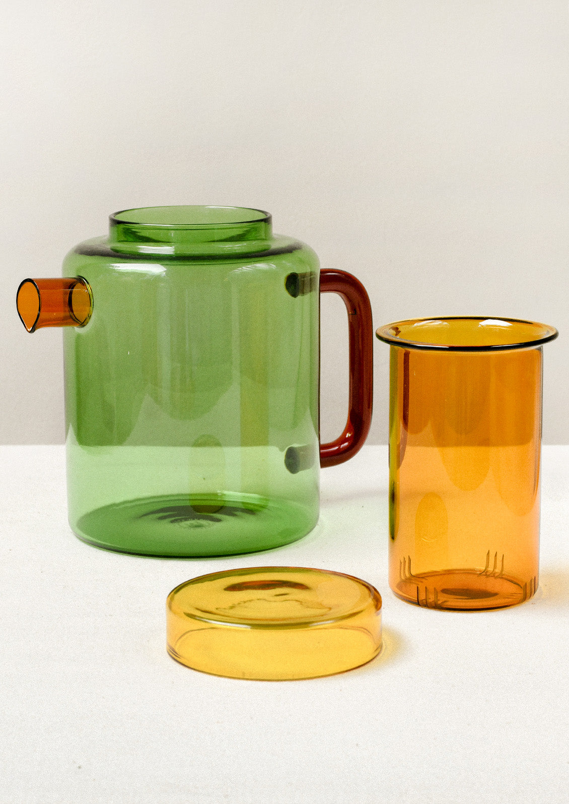 A multicolored glass teapot with agreen body, an orange spout, red handle, and removable yellow tea steeper.