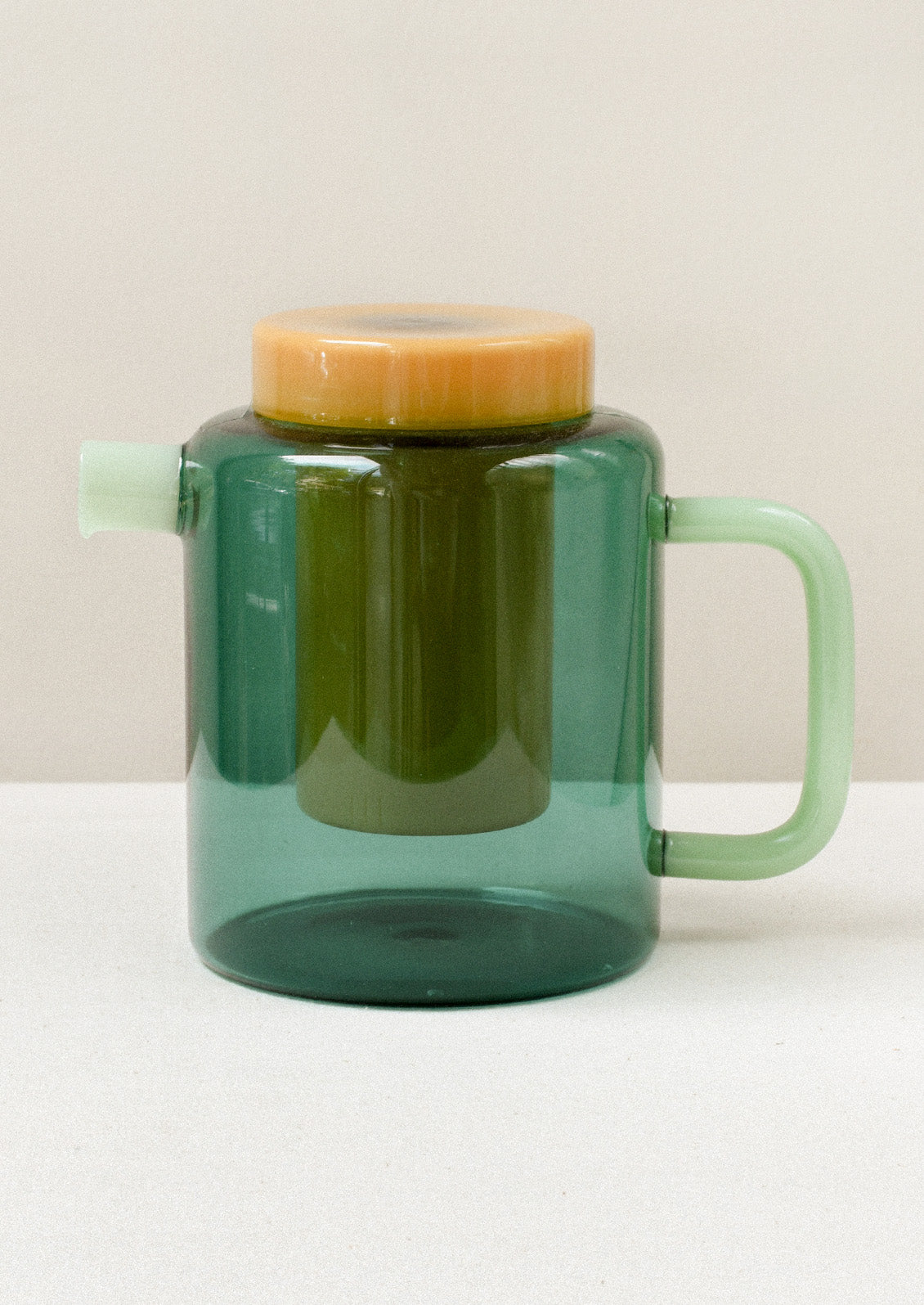 A multicolored glass teapot with a teal body, mint green spout and handle, and removable yellow tea steeper.