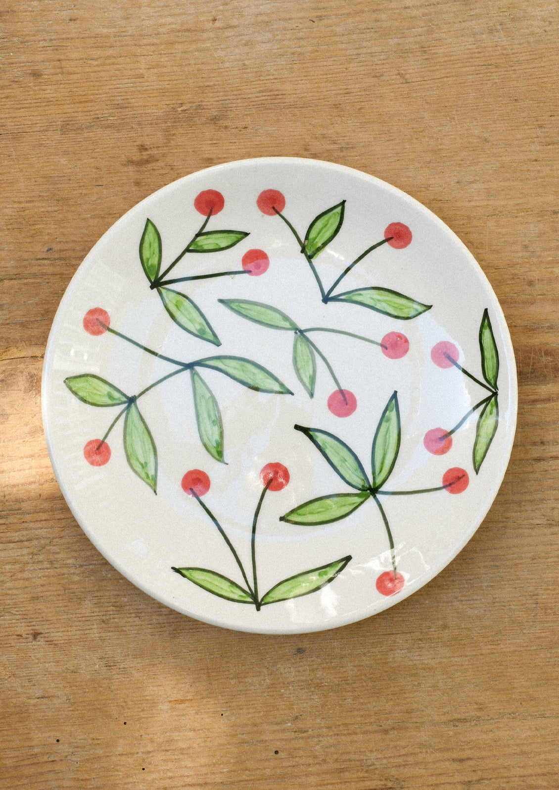 A ceramic plate with illustrated red cherries.