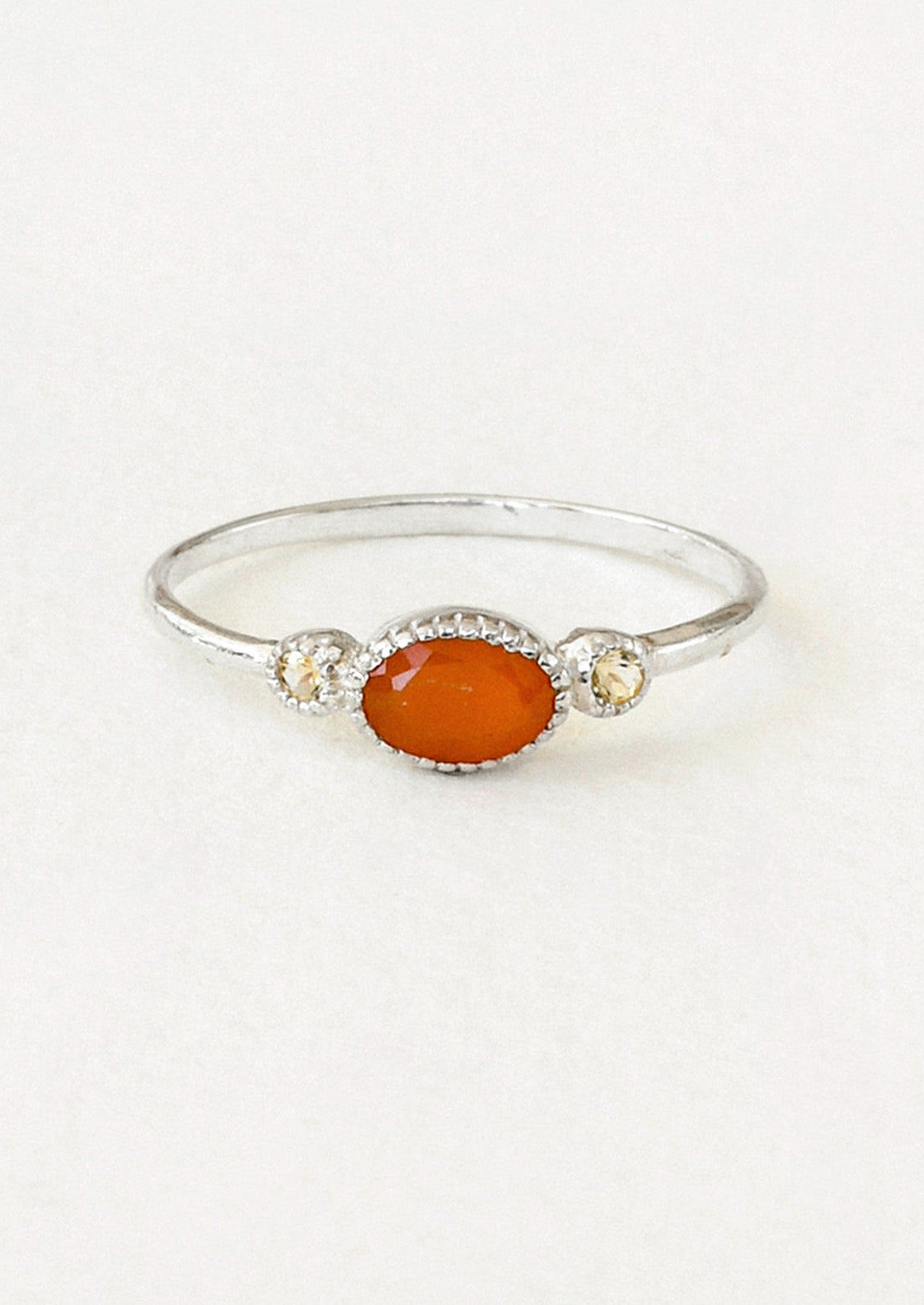 A sterling silver ring with a carnelian oval in the center framed by two small round citrine stones on either side.