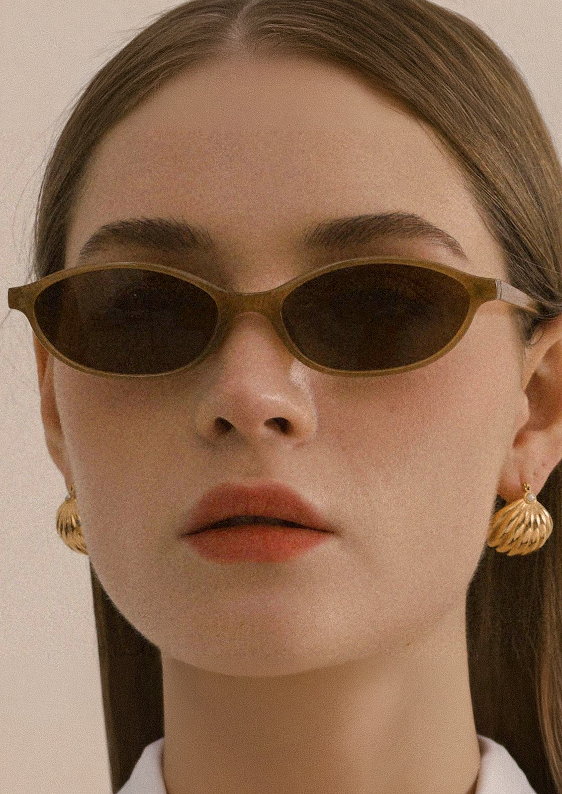 A woman wearing a pair of oval sunglasses with honey brown frames and brown tinted lenses.
