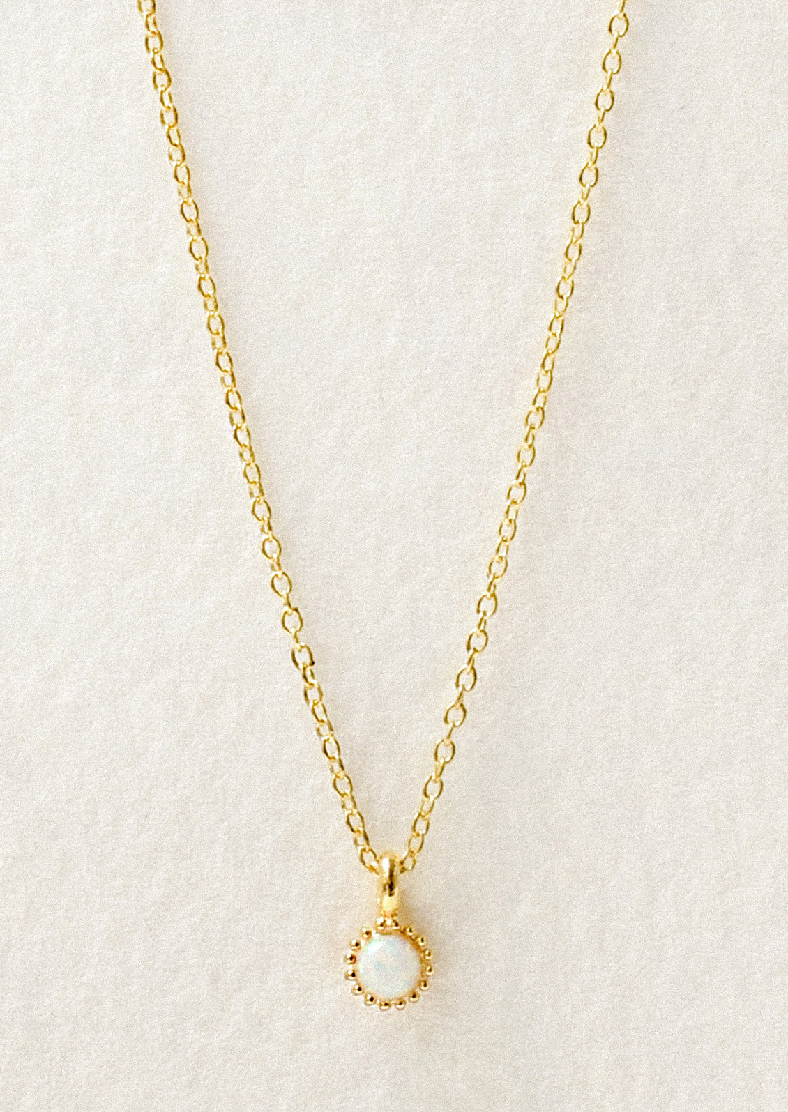 A dainty gold necklace with a small simulated opal charm.