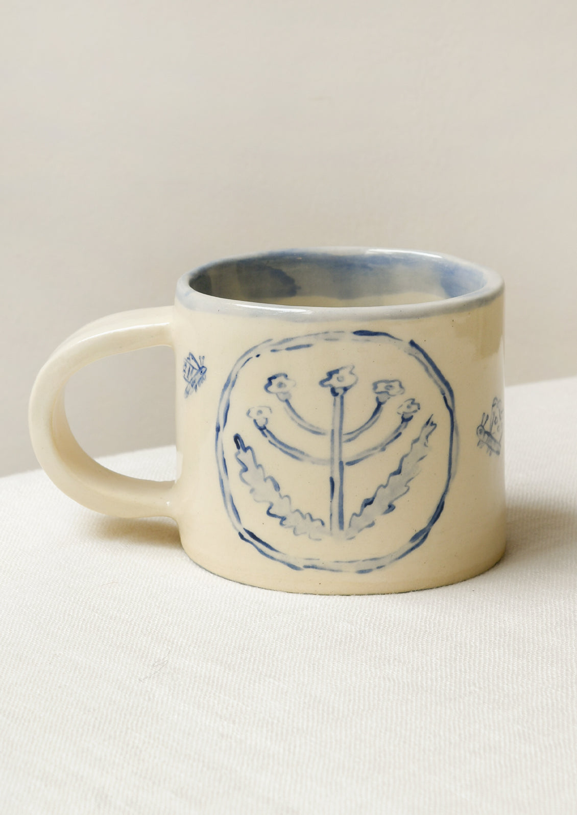 A handmade ceramic mug with illustrations of flowers and tiny insects on the outside and a gingham pattern on the inside.