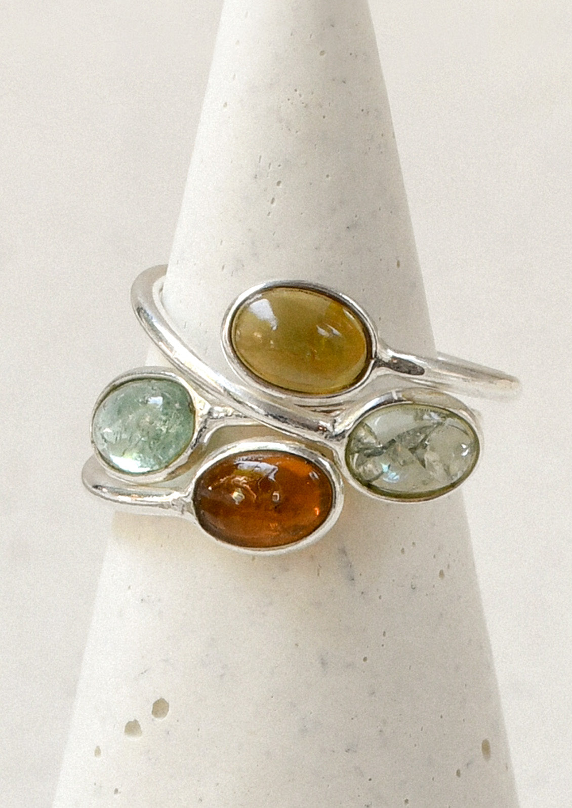 Two sterling silver rings with a wrapped design and stacked natural tourmaline stones in varying hues.