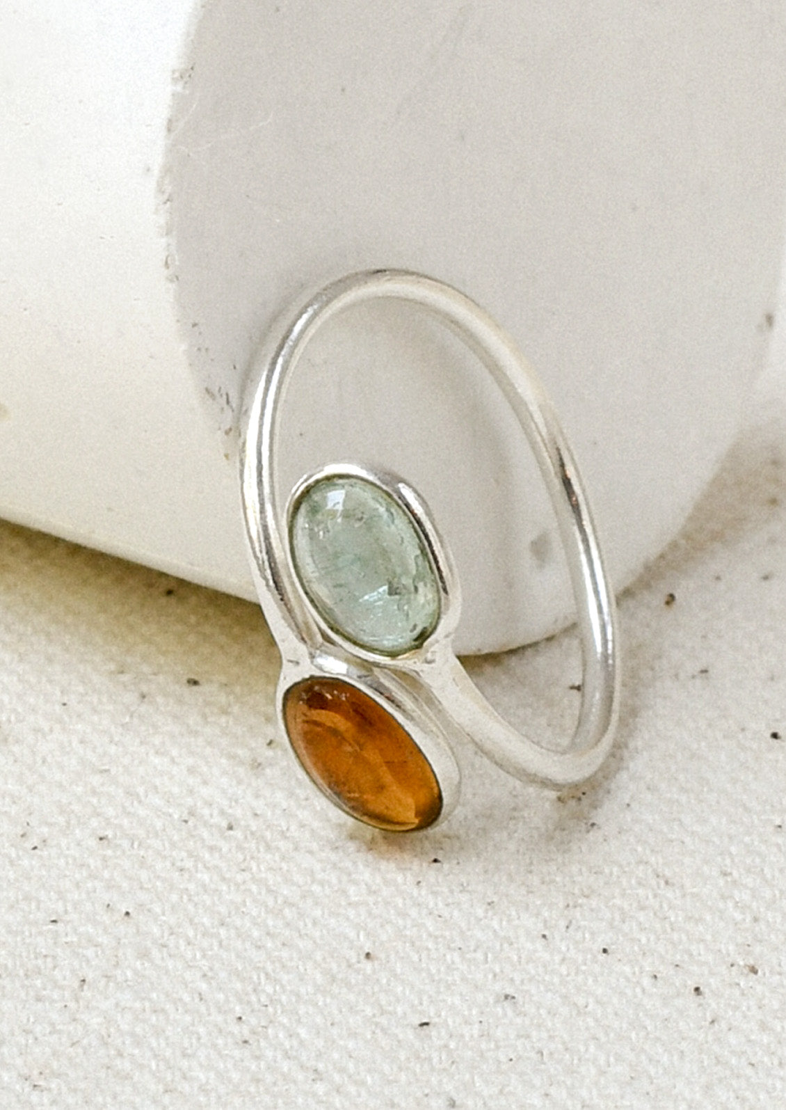 A sterling silver ring with a wrapped design and two stacked natural tourmaline stones leaning against a white object.