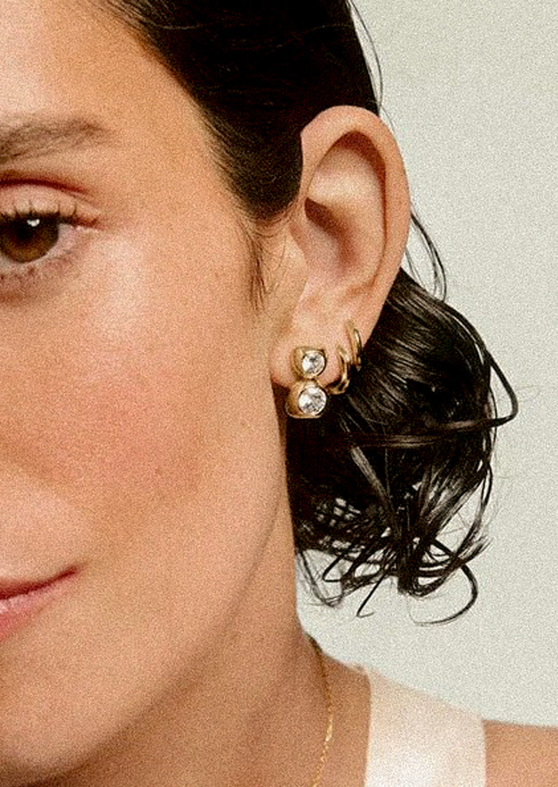 A woman wearing two gold hoop earrings and a gold duo bezel stud earring.