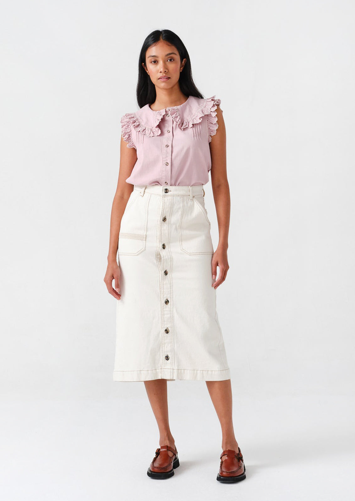 A woman wearing a white denim midi skirt, lilac top, and loafers. 