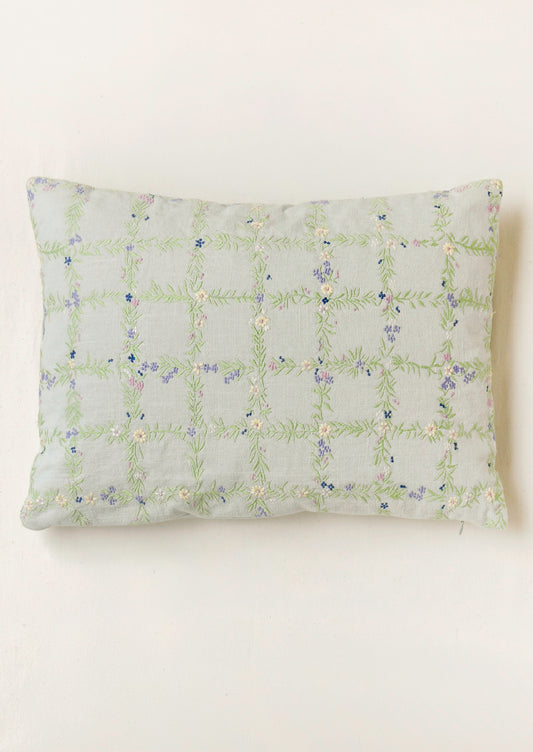 A light blue pillow with an embroidered floral grid pattern.