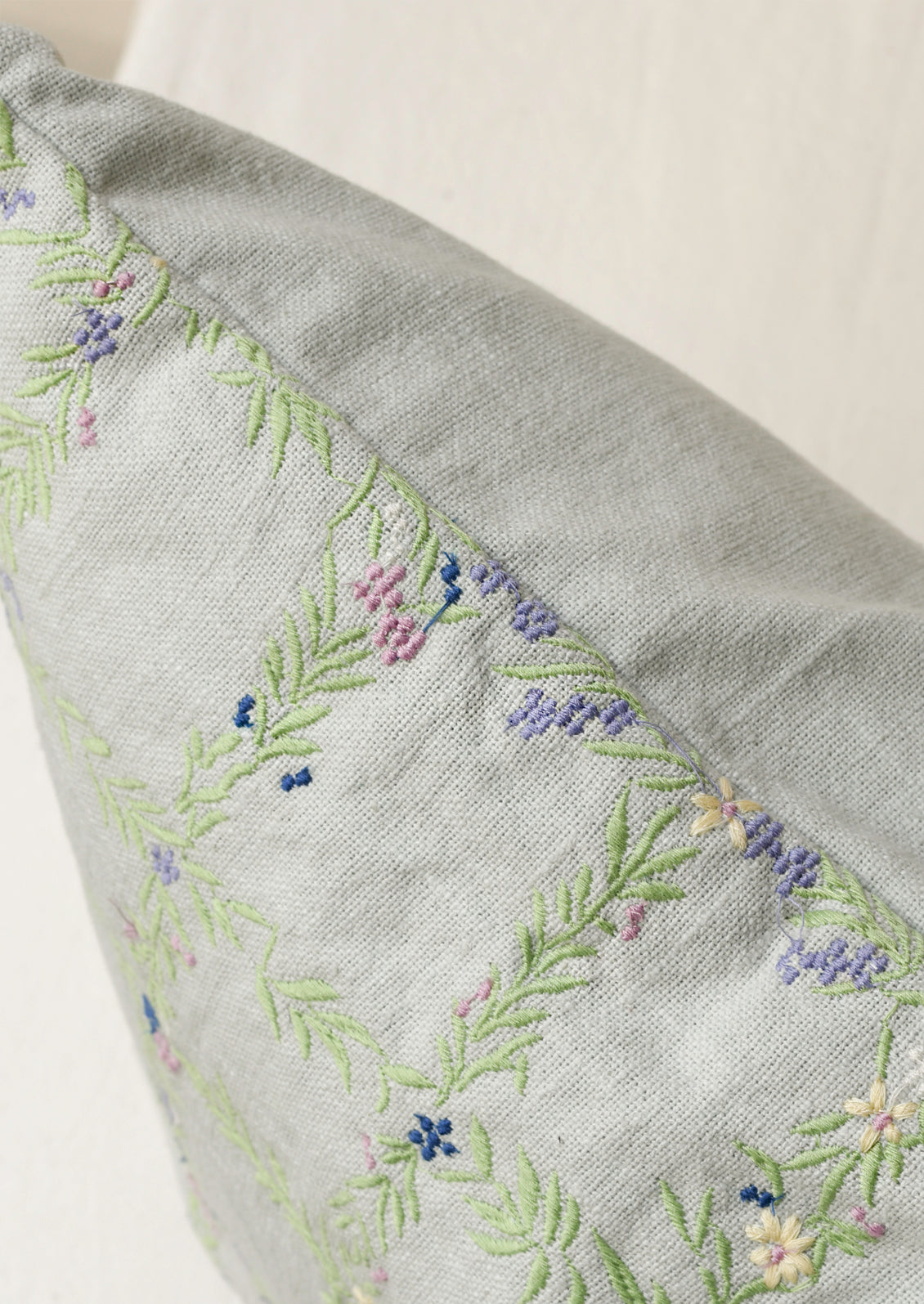 Closeup of a light blue pillow with an embroidered floral grid pattern.