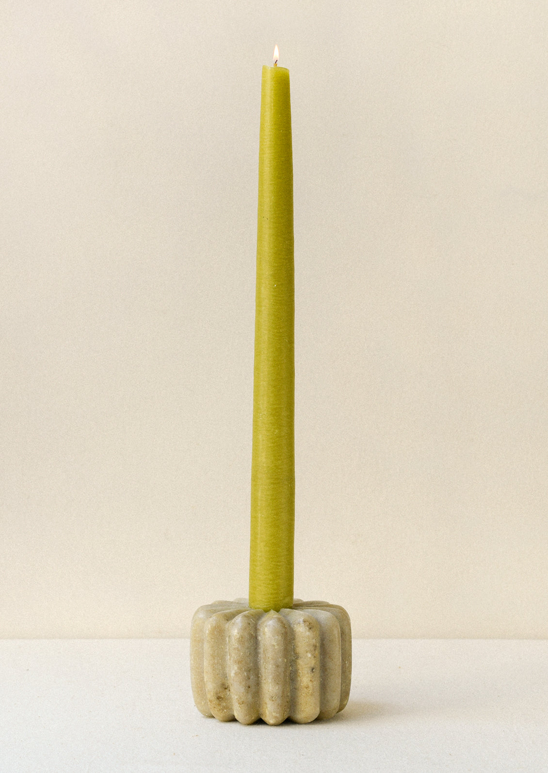 A fluted marble taper holder with a long green taper candle.