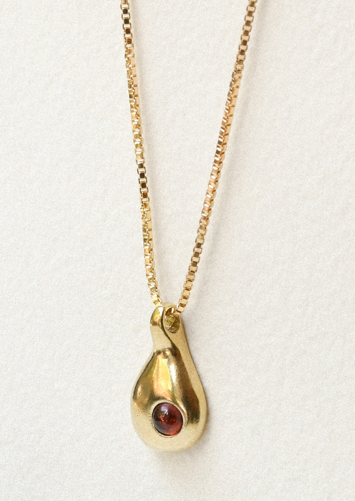 A bronze necklace with a droplet charm with a garnet on the front.