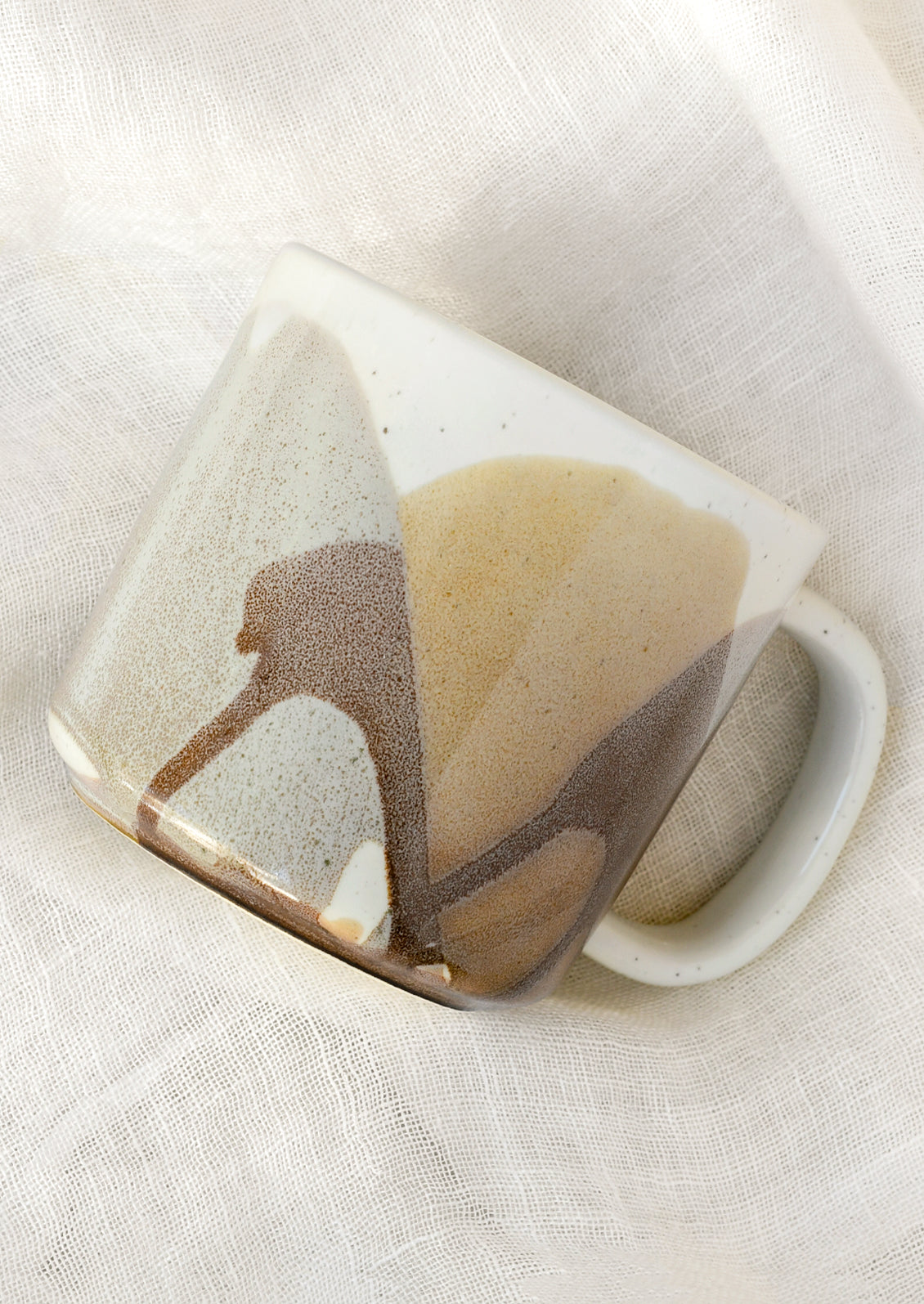 A white ceramic mug with a painted abstract design in brown and grey.