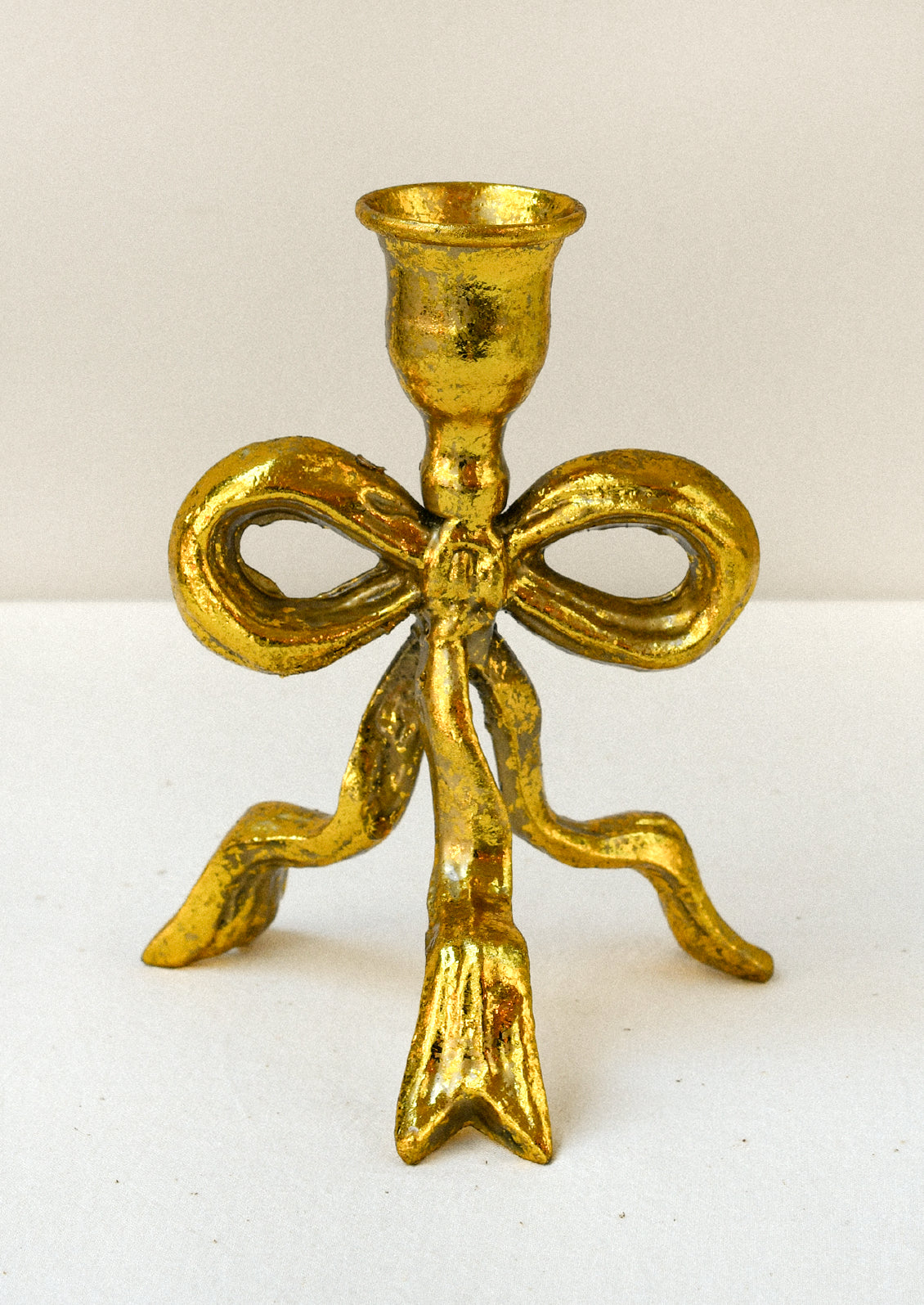 A metal taper holder in the shape of a bow with a gold finish.