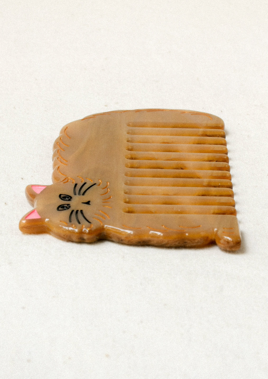 Side view of a caramel colored hair comb in the shape of a cat.